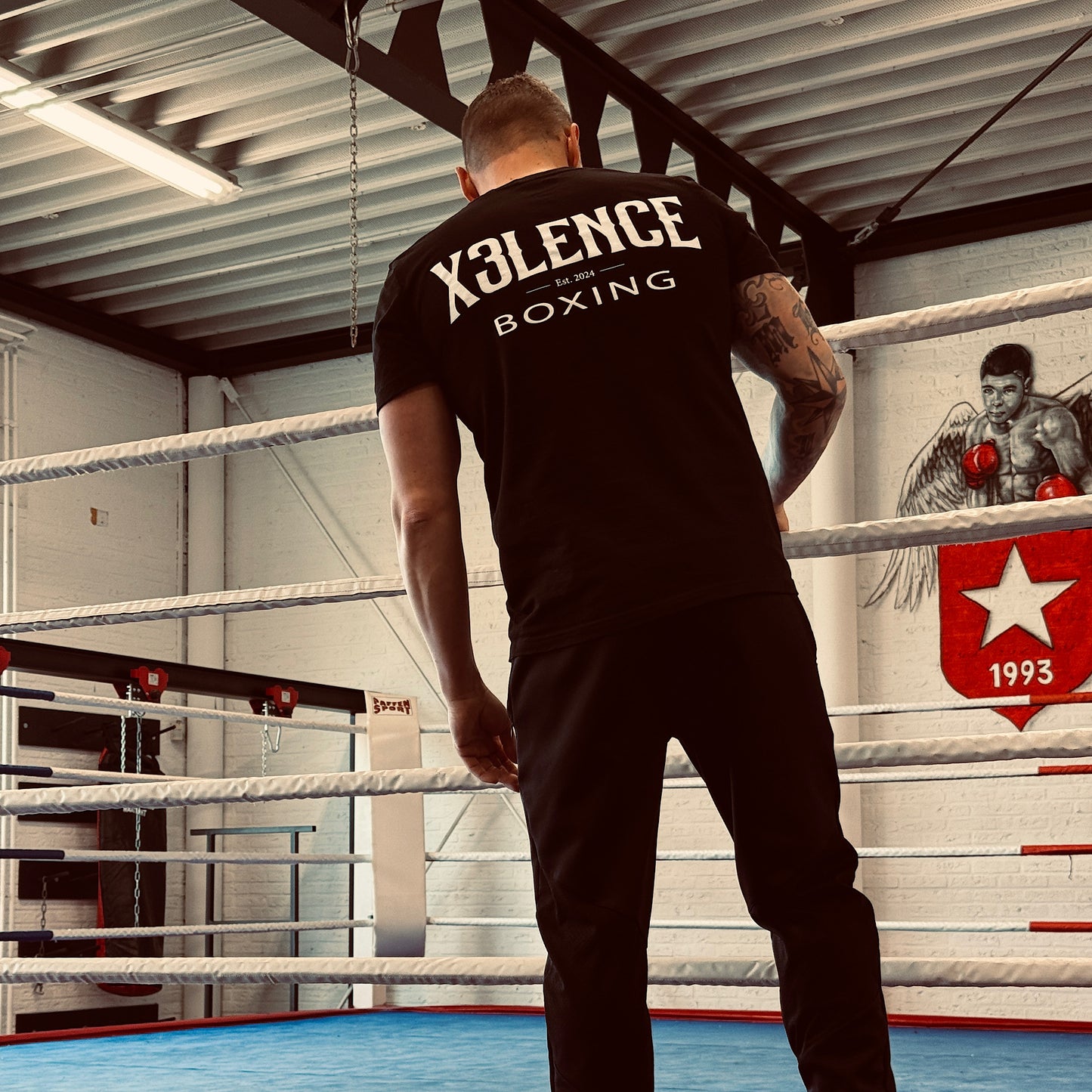 Man in de ring met het zwarte X3LENCE T-shirt – groot wit logo “X3LENCE BOXING” op de rug zichtbaar, krachtige uitstraling in een bokssfeer.